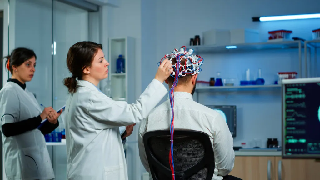 Back View Man Patient Wearing Performant Brainwave Scanning Headset Sitting Neurological Research Laboratory While Medical Researcher Adjusting It Examining Nervous System Typing Tablet