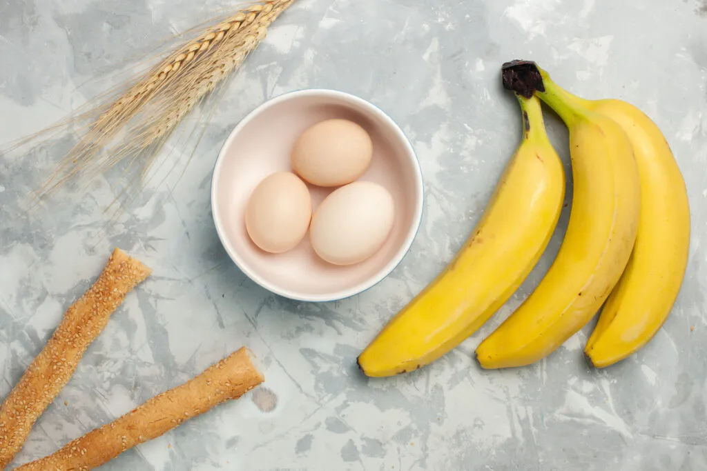 Top View Yellow Bananas With Raw Eggs Bun Bread Light White Desk